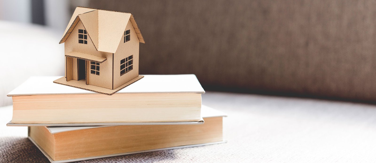 Pila de libros con una casa de juguete encima, simbolizando el directorio de agencias literarias en España para ayudar a un autor a encontrar la representación adecuada para su libro.