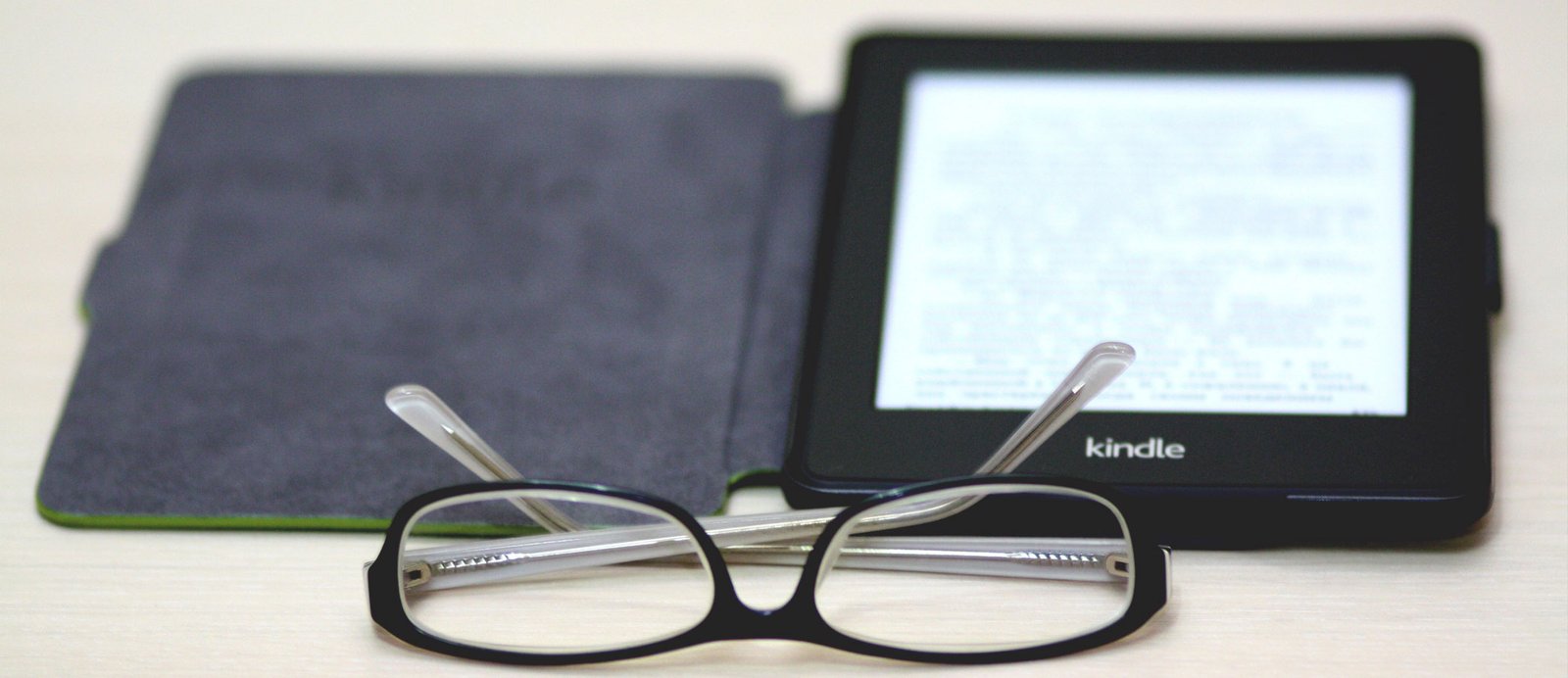 Imagen de un e-reader kindle abierto, en el que se visualiza un e-book, y unas gafas al lado.