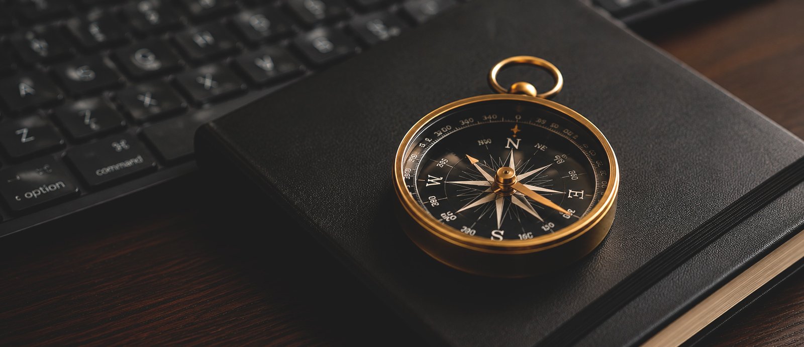 Una brújula de bronce apoyada sobre un cuaderno negro cerrado junto a un teclado de ordenador, simbolizando el propósito de autor como guía estratégica.