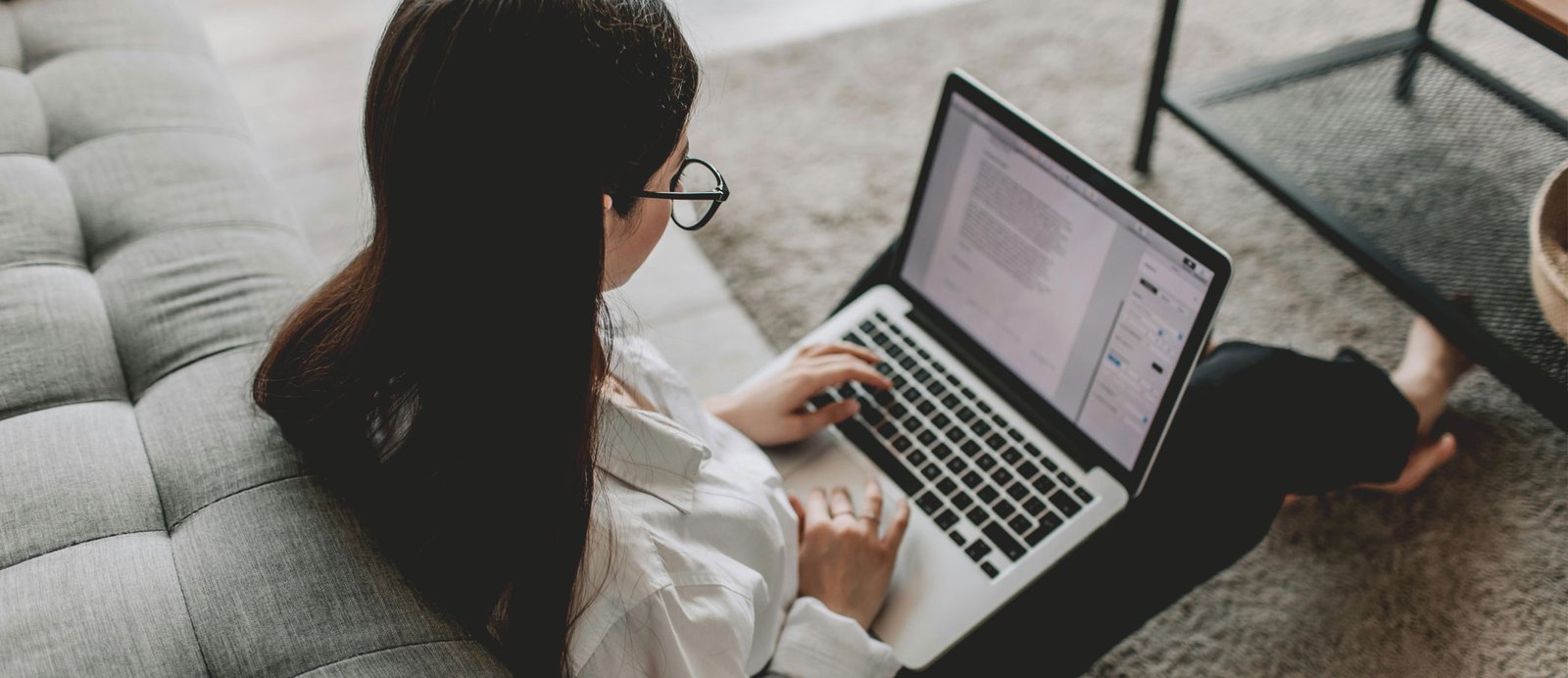 Una escritora sentada en la alfombra de su salón, redactando concentrada en su portátil una carta de presentación para una editorial.