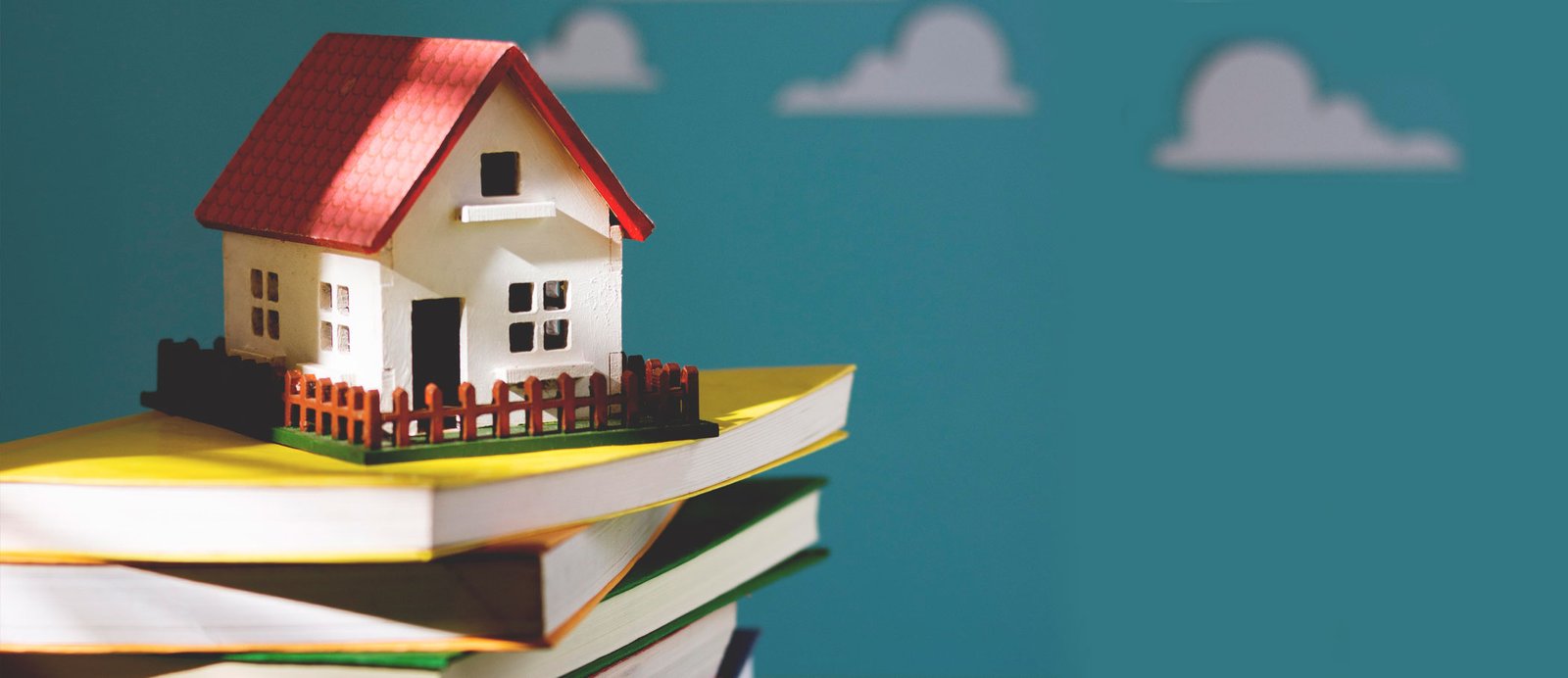 Pila de libros con una casa de juguete encima, representando la búsqueda de una dirección física o de correo electrónico a través de los directorios de editoriales y agencias literarias.