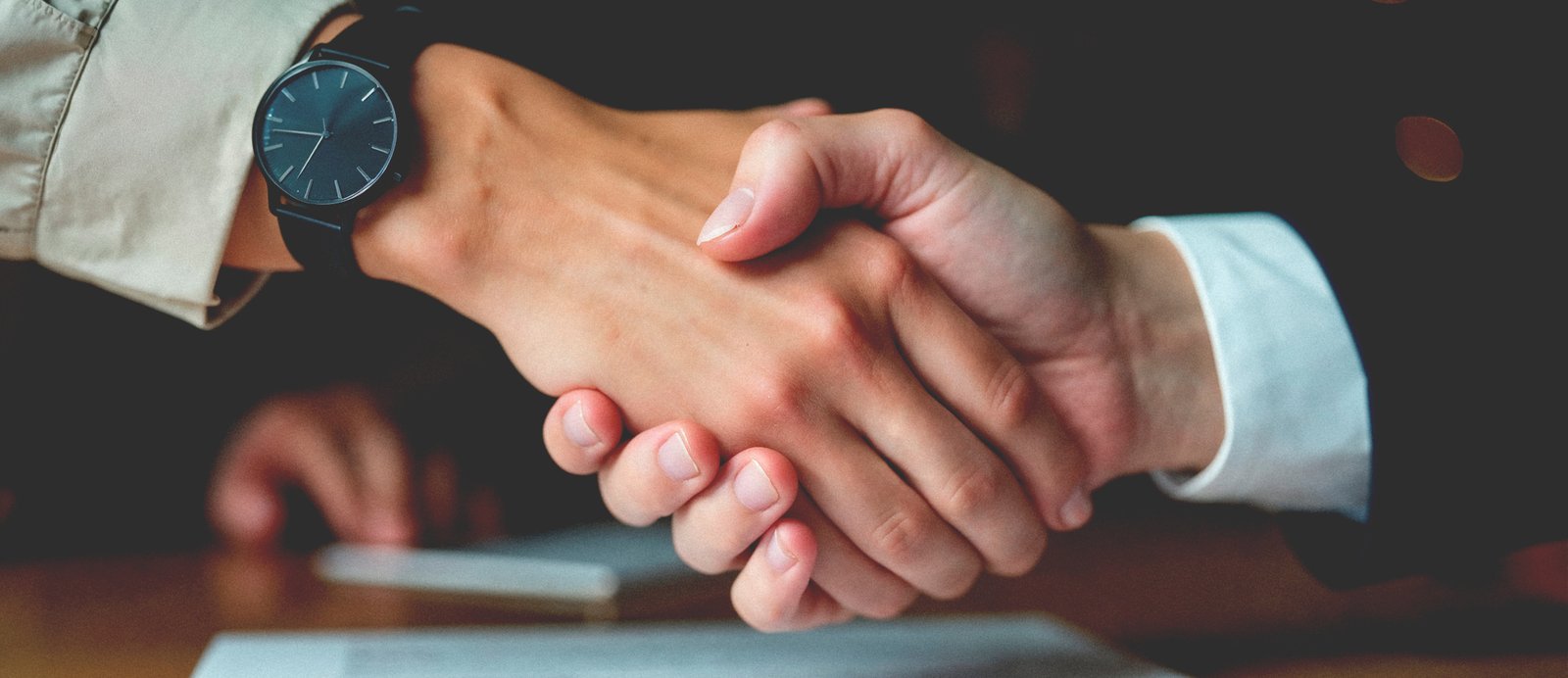 Dos manos estrechándose tras formalizar por escrito un contrato de edición según la Ley de Propiedad Intelectual.