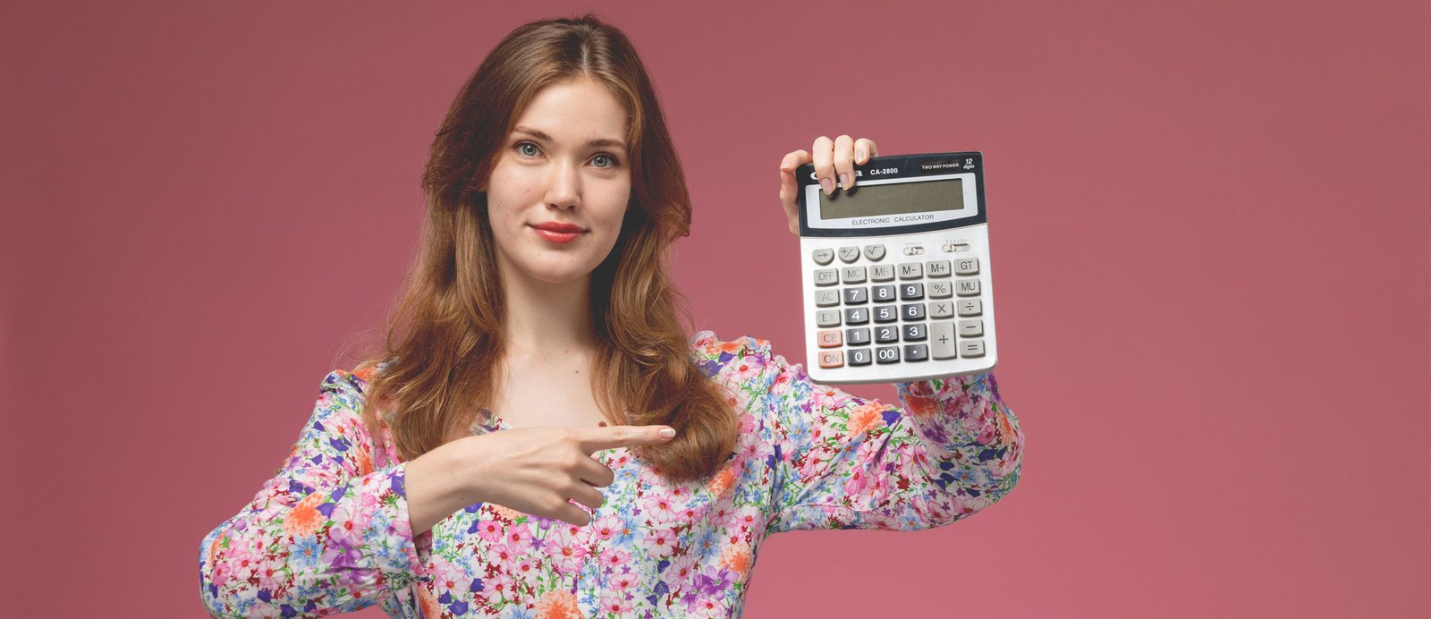 El objetivo de este cálculo: saber cuánto dinero te queda realmente en el bolsillo después de impuestos. Una mujer sonriente señala una calculadora, ilustrando un caso práctico sobre la fiscalidad de los derechos de autor.