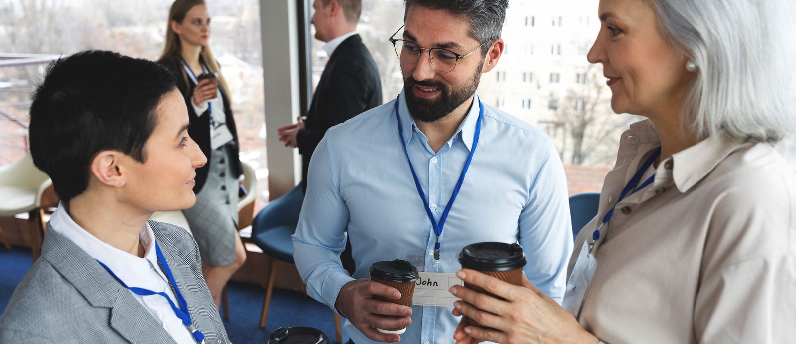 El networking y las relaciones personales en la feria son el motor que activa las ofertas y las subastas. Tres profesionales del sector editorial conversando con sus tarjetas de acreditación visibles, ilustrando el networking informal entre agentes, editores y scouts.