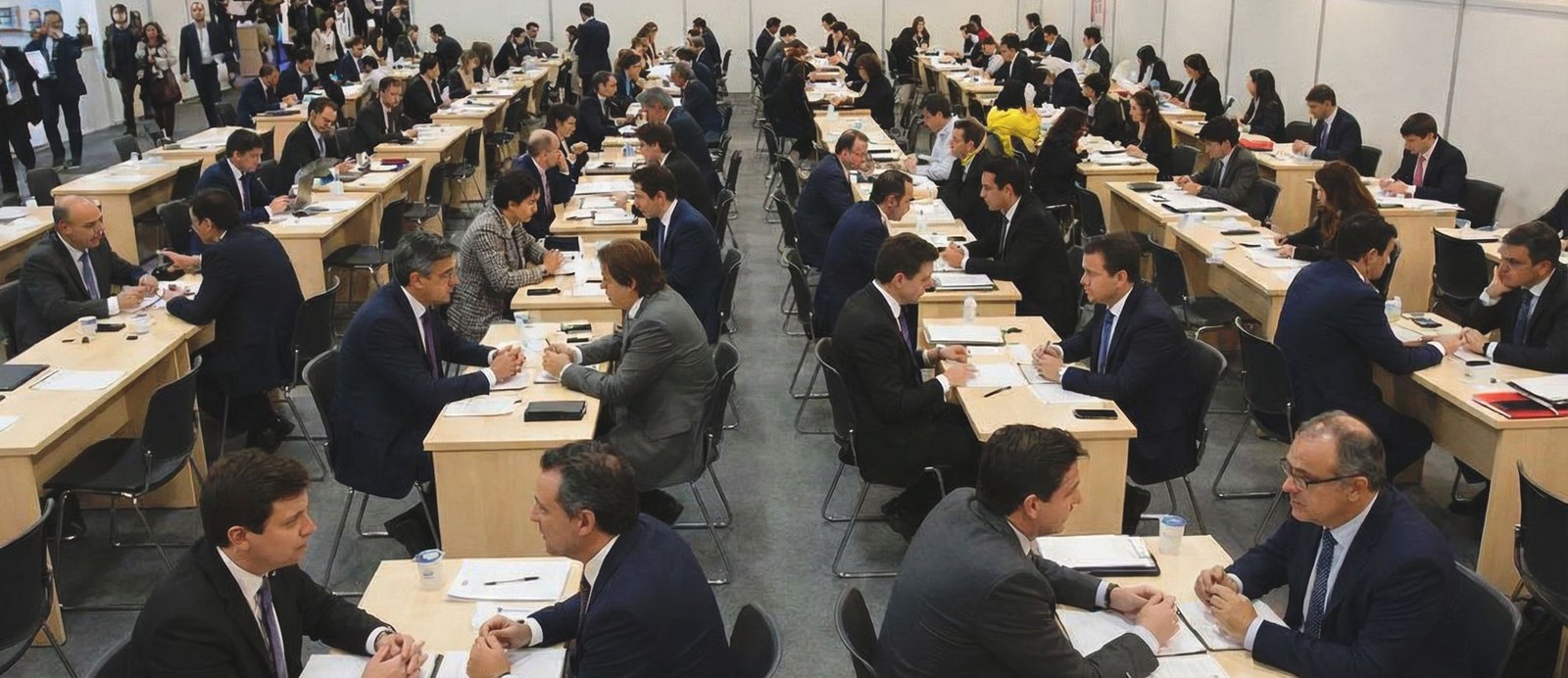 El 'speed dating' editorial: cientos de reuniones cronometradas en un entorno austero y profesional, lejos del glamour de la feria. Vista interior del inmenso pabellón de negociación de una feria del libro, repleto de filas interminables de mesas pequeñas y numeradas, donde cientos de agentes y editores realizan reuniones de negociación simultáneas cara a cara para la compraventa de derechos.
