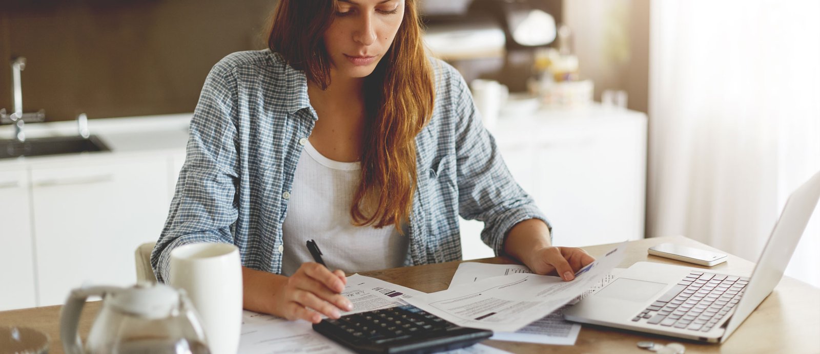 El secreto del autor-emprendedor: un registro impecable de ingresos y gastos para que estos números cuadren. Una autora autoeditada en su escritorio, revisando papeles y usando una calculadora para sus impuestos trimestrales.