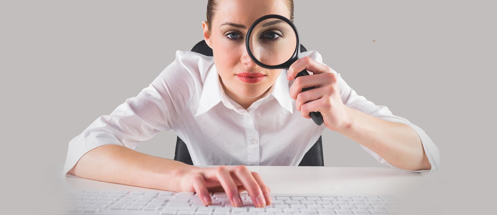 Una mujer con una lupa investigando por Internet delante de su pc, simbolizando el análisis que el autor debe hacer de editoriales y agencias para asegurarse de que su obra tendrá un sitio en su catálogo.