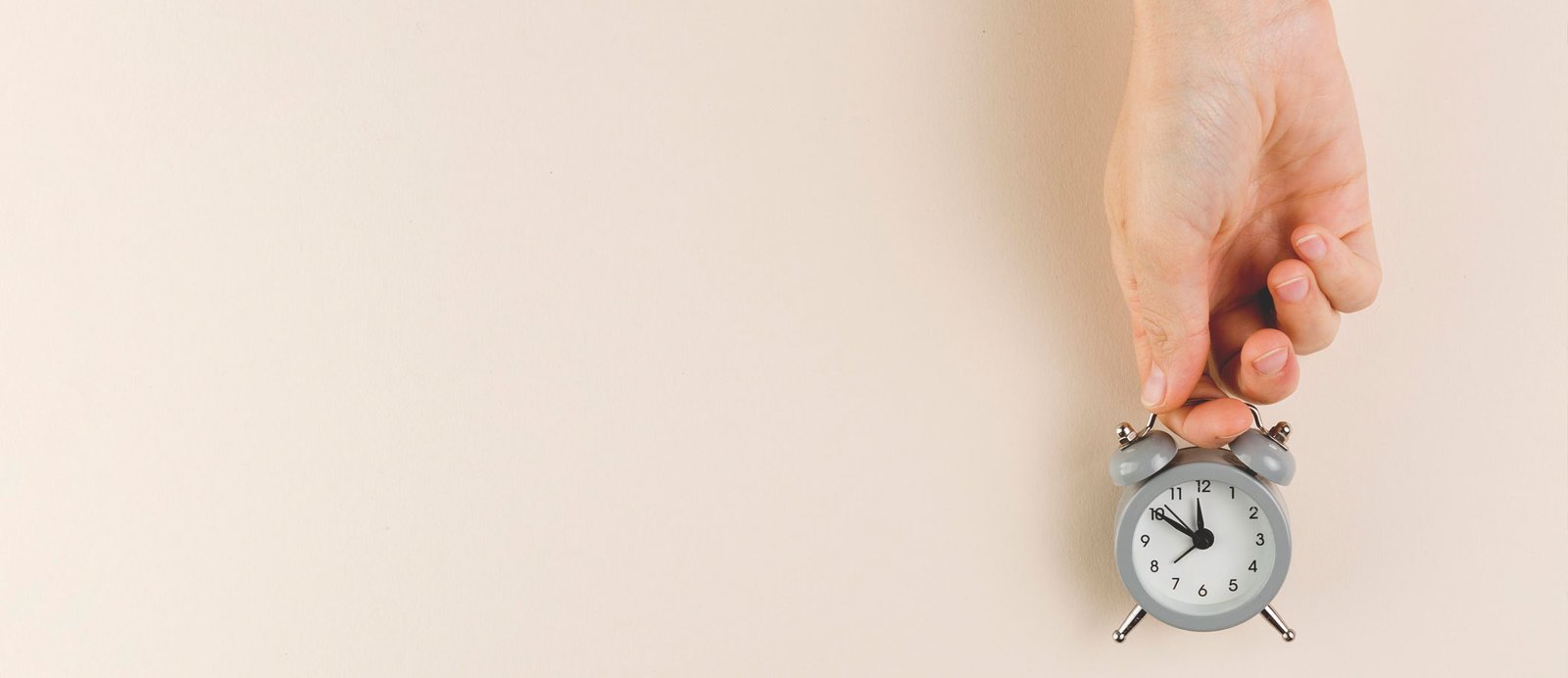 Una mano sujetando un reloj de mesa, simbolizando el tiempo de espera para recibir una respuesta de una editorial o agente literario.