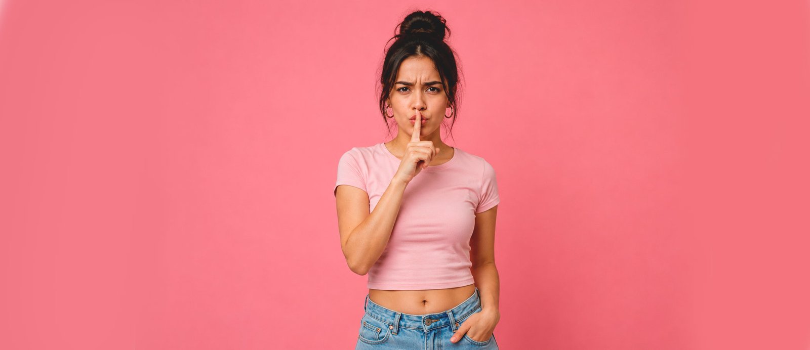 ¡Shhh! Es hora de silenciar a tu crítico interno y dejar que la historia fluya. Joven con camiseta rosa haciendo el gesto de pedir silencio con el dedo sobre los labios, representando la acción de callar la voz autocrítica del escritor.