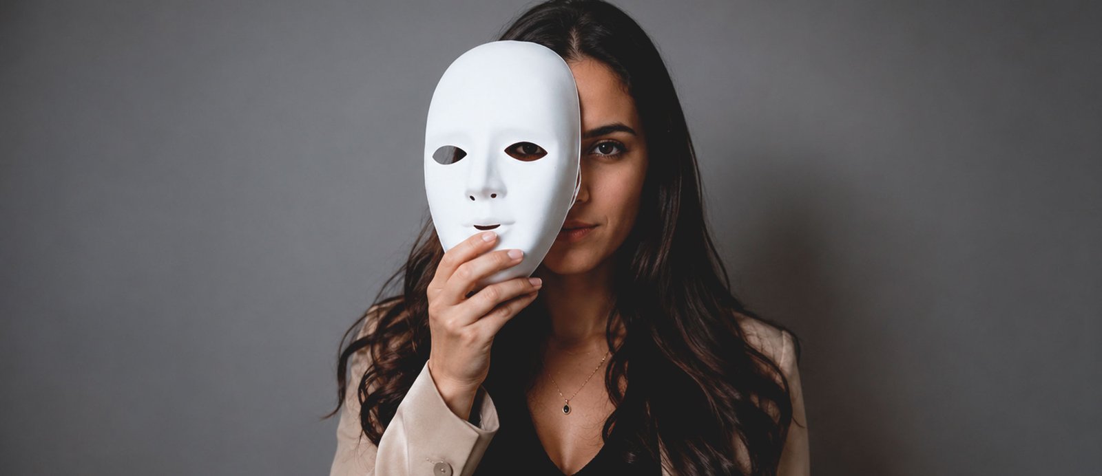 Guía de supervivencia para escritores: cómo cruzar el «valle de la muerte» de tu novela. Imagen de una mujer con una máscara blanca frente a su cara, ilustrando el síndrome del impostor y el bloqueo del escritor en el proceso creativo.